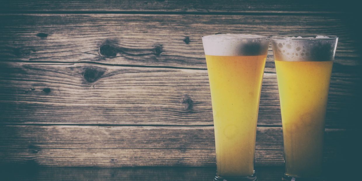 Two frothy glasses of beer against a rustic wooden background.