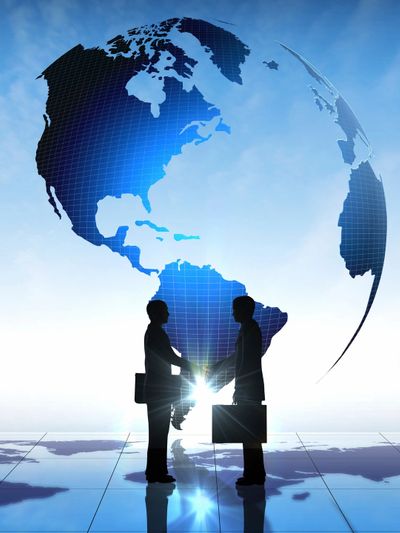Two businesspeople shaking hands with a digital globe in the background.