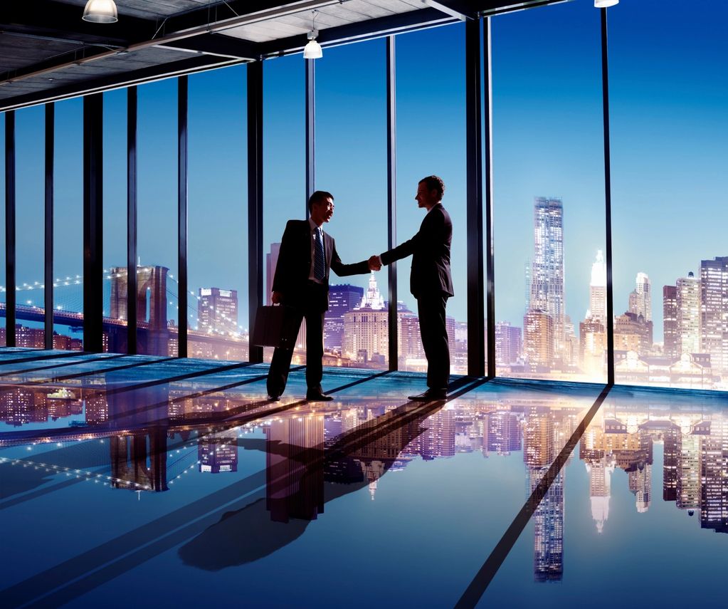 Two businessmen shaking hands in a modern office with city skyline views.