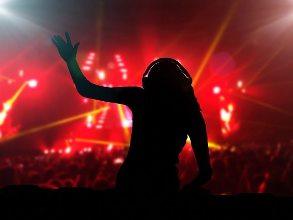 Silhouette of a person dancing at a vibrant concert with red and yellow lights.