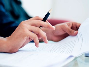 Person reviewing documents with a pen in hand.