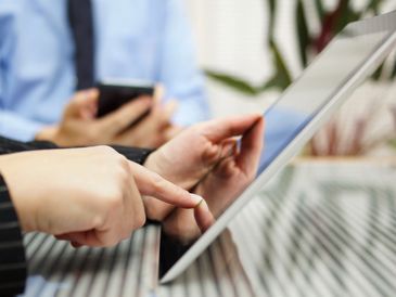 Two people using a tablet and smartphone at a table.