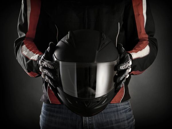 Person holding a black motorcycle helmet wearing gloves and a jacket.