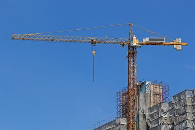 Tall crane at construction site against a clear blue sky.