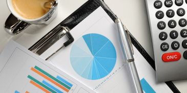Workspace with coffee, charts, pen, and calculator on a white desk.
