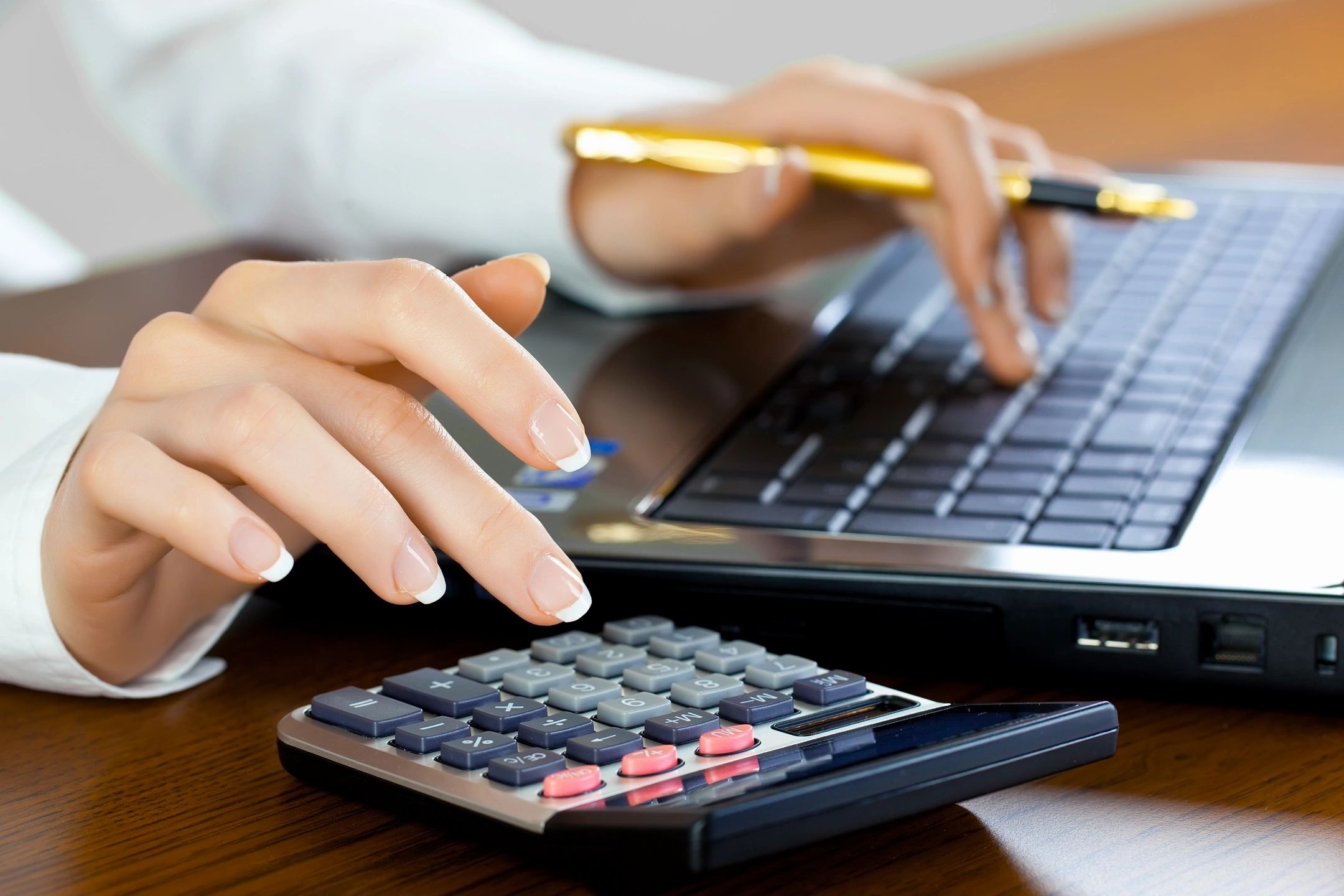 Person sitting at computer and calculating numbers on calculator.