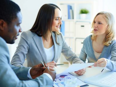 Three professionals discussing documents in a bright office.