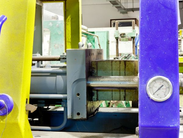 Close-up of industrial machinery with yellow and blue parts and a pressure gauge.