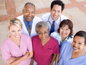 A diverse group of smiling healthcare professionals in scrubs and lab coats.