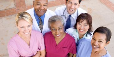Diverse group of smiling healthcare professionals in scrubs and lab coats.