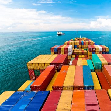 Cargo ship loaded with colorful shipping containers sailing on blue ocean under a partly cloudy sky.