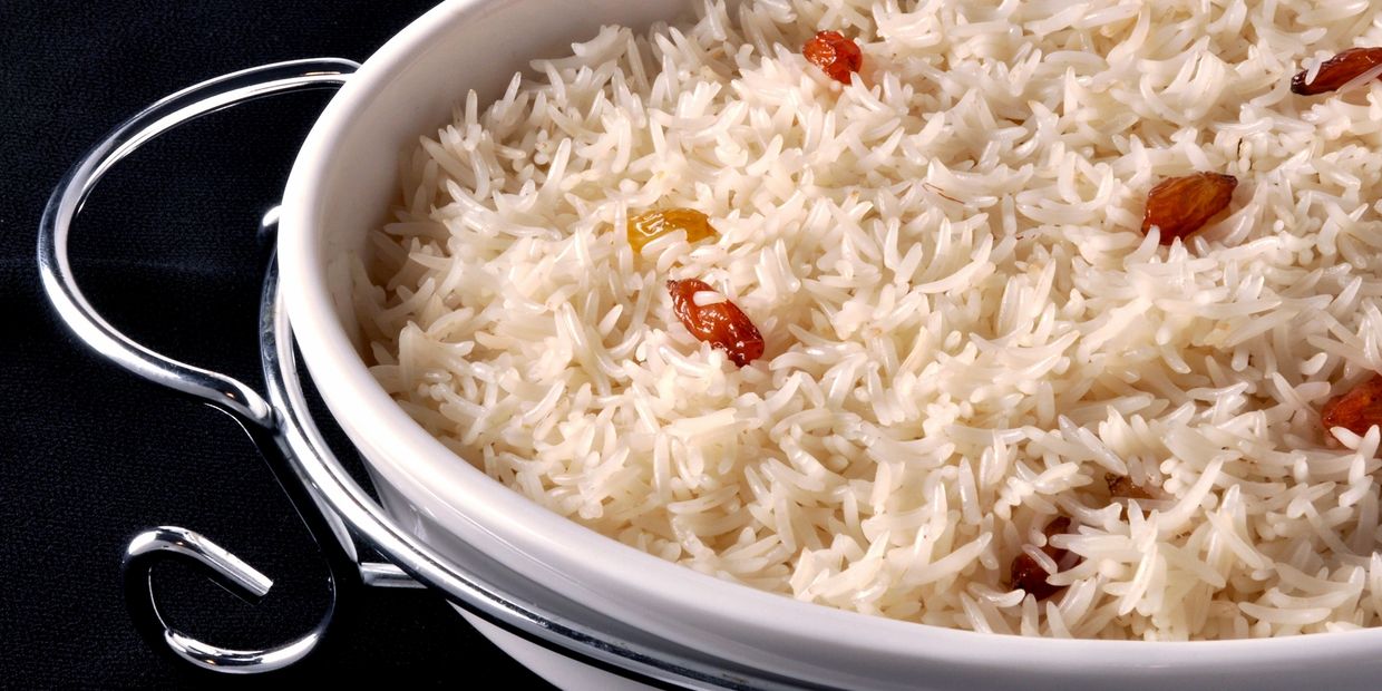 Basmati rice garnished with raisins in a white serving dish with metal handles.