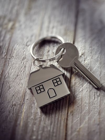 A silver house-shaped keychain with a key on a wooden surface.