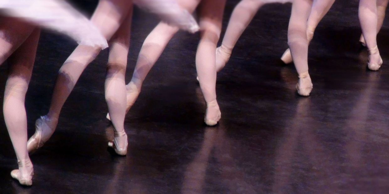 Ballet dancers performing en pointe on stage with leg movements.