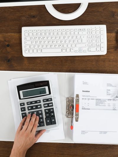 Person using calculator with invoice and keyboard on desk.