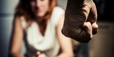 A clenched fist in the foreground with a distressed woman blurred in the background.