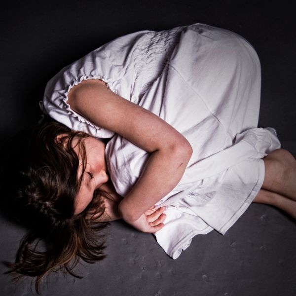 Woman curled up on the ground in white dress.