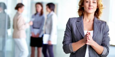 Confident businesswoman stands in focus with colleagues blurred in background.