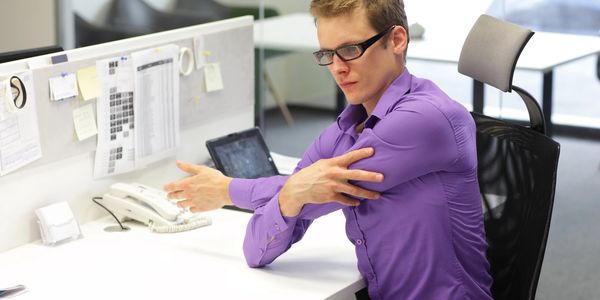 Man in purple shirt stretching his arm at office desk.