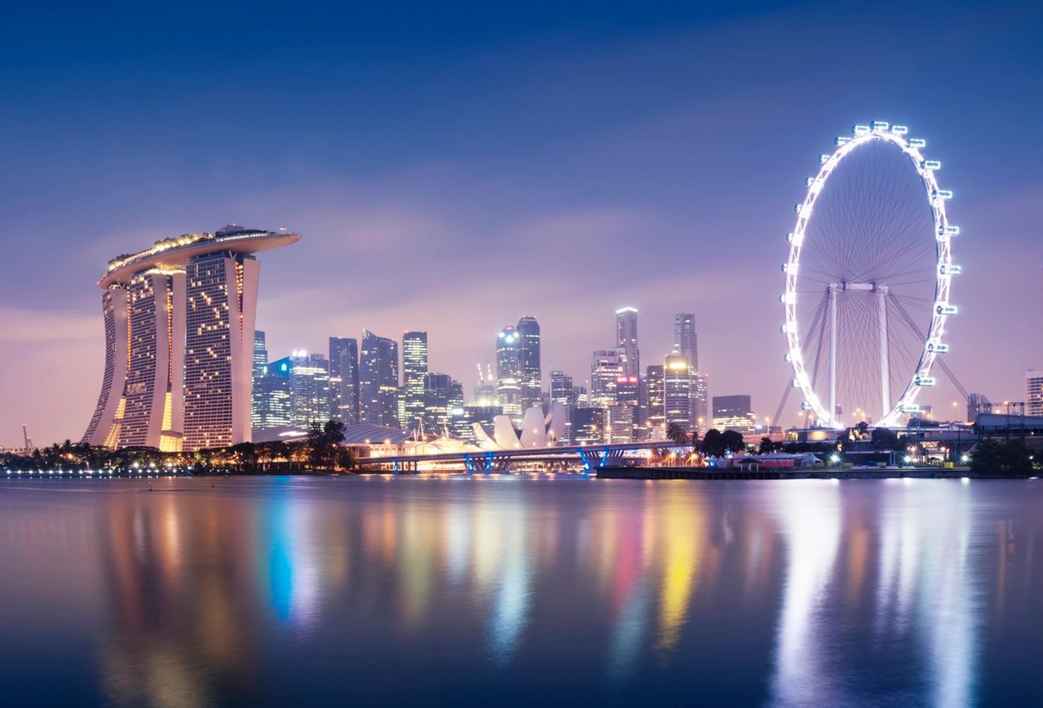 Night view of Singapore skyline with Marina Bay Sands and Singapore Flyer reflected in water.
