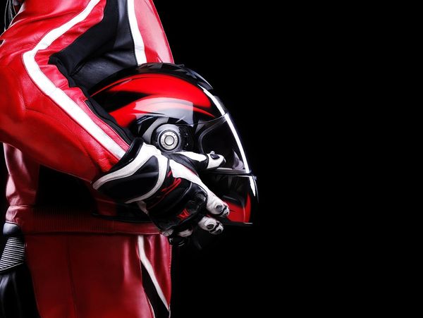 Motorcyclist in red gear holding a matching red and black helmet against a black background.