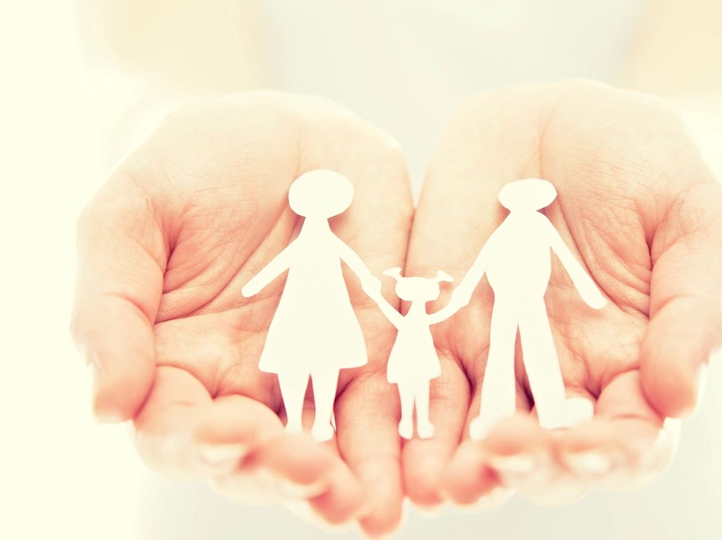 Hands holding paper cutouts of a family, symbolizing care and protection.