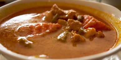 A bowl of creamy curry with vegetables and meat.