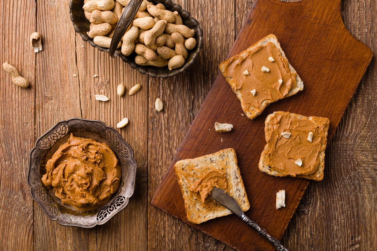 Rustic wooden table setting with whole peanuts, creamy peanut butter, and multigrain toast—ideal for protein-packed snacks, clean eating, or healthy breakfast ideas.