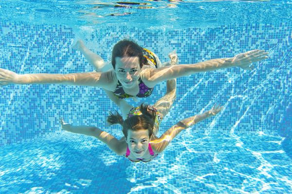 Two girls swimming underwater in a pool with outstretched arms.