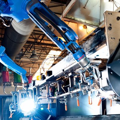 Blue robotic arm welding metal in an industrial factory setting.