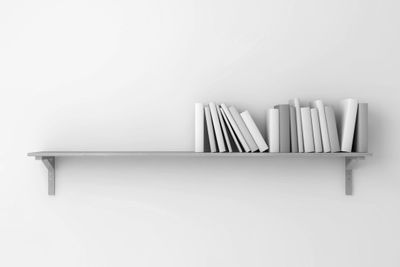 Minimalist white shelf with white books arranged on a white wall.