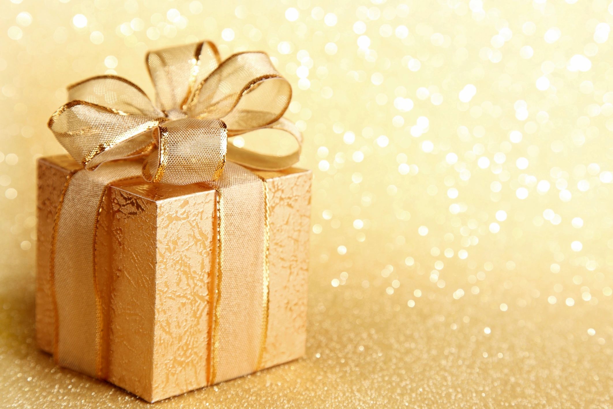 Elegant gold gift box with shimmering ribbon against sparkling background.
