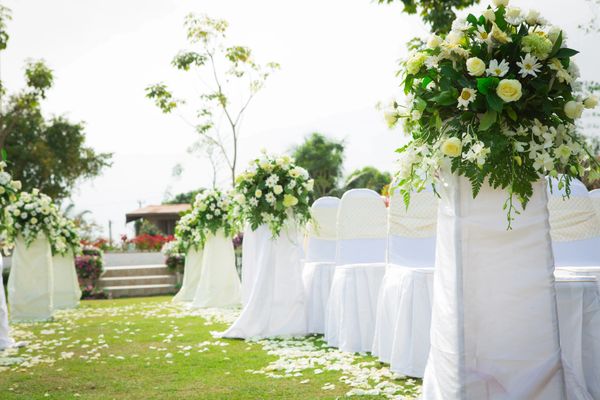Outdoor wedding setup with white chairs and floral decorations.