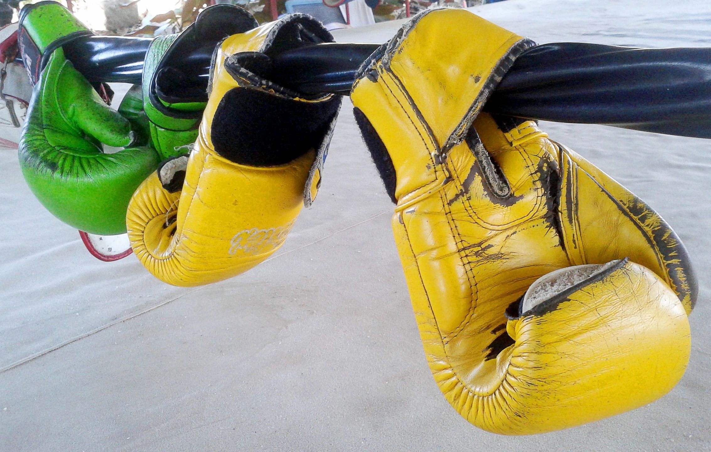Worn yellow and green boxing gloves hanging on a black bar.