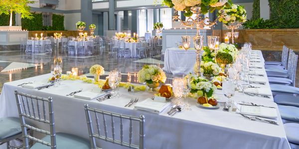 Elegant banquet tables set with white linens, flowers, and candles in a spacious venue.