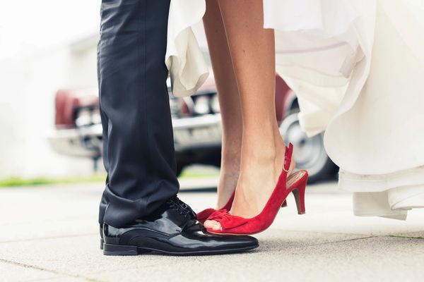 Close-up of a bride's red heels touching a groom's shiny black shoes.