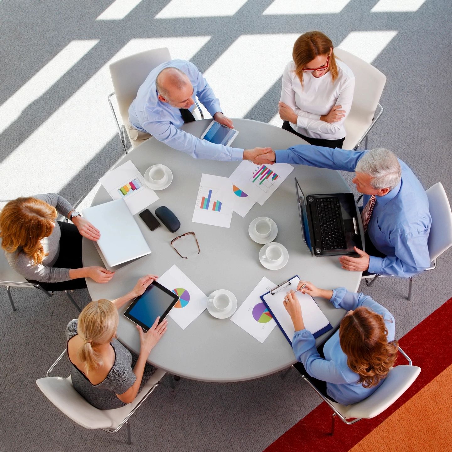 Business meeting with professionals shaking hands around a table with charts and devices.