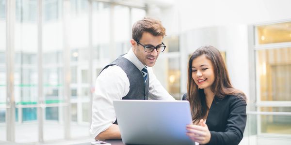 Jeune homme et jeune femme dans un bureau sourient devant un ordinateur portatif