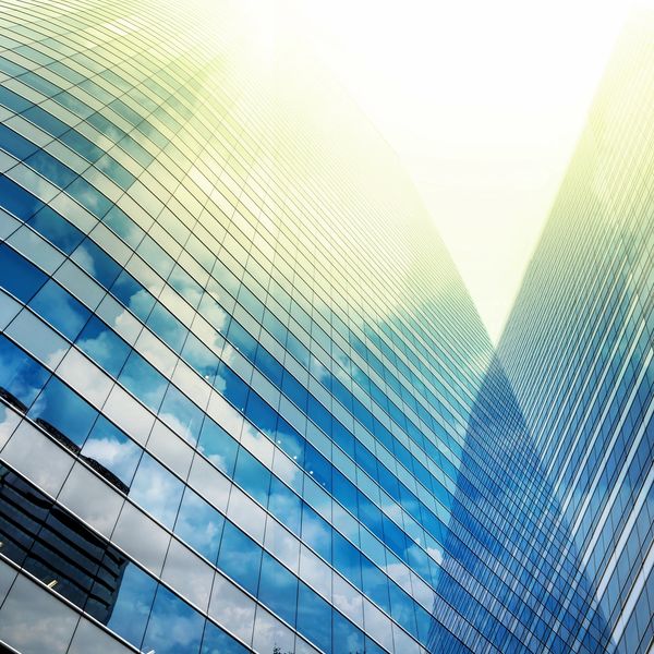 Sunlit glass skyscrapers reflecting the blue sky and clouds.