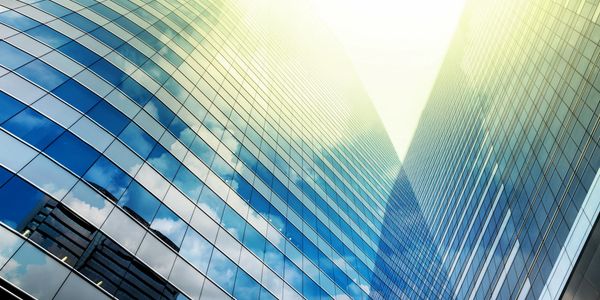 Photo looking up between two glass office blocks with Sun Shine beaming down between them.