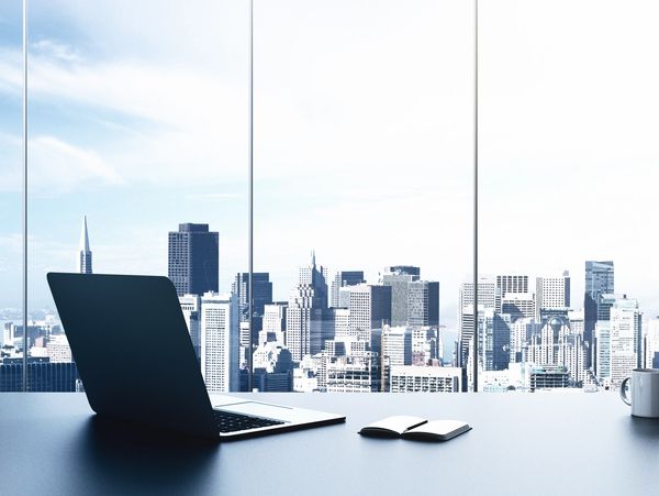 Modern office desk with laptop and notebook overlooking city skyline.