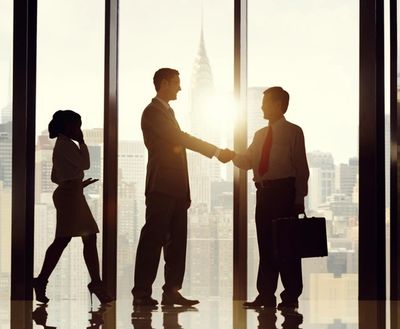 Two businessmen shaking hands with a city skyline in the background.