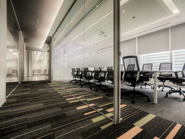 Modern office corridor with glass-walled conference room and stylish chairs.