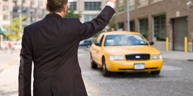 Man in suit hailing a yellow taxi on a city street.