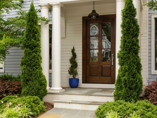 Elegant porch entrance with wooden door and manicured greenery.