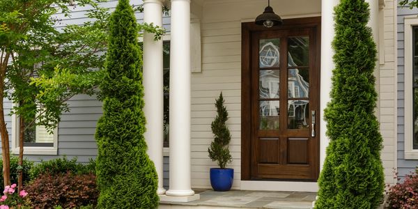 Elegant house entrance with white columns and greenery.