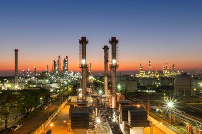Oil refinery at sunset with illuminated towers and industrial structures.