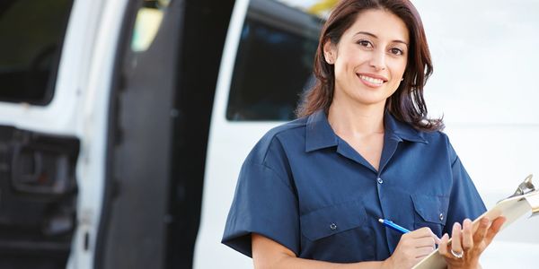 Smiling delivery woman in uniform holding clipboard by van.