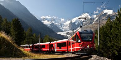 A red train traveling through mountainous terrain with snowy peaks.