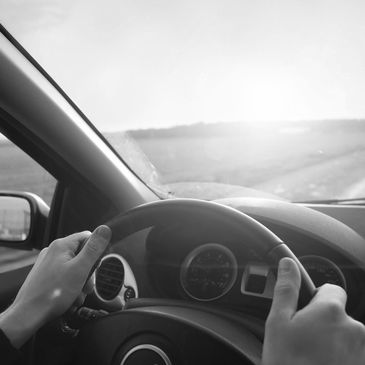 Woman driving car to get it cleaned and both hands on wheel driving down the road toward sunrise.